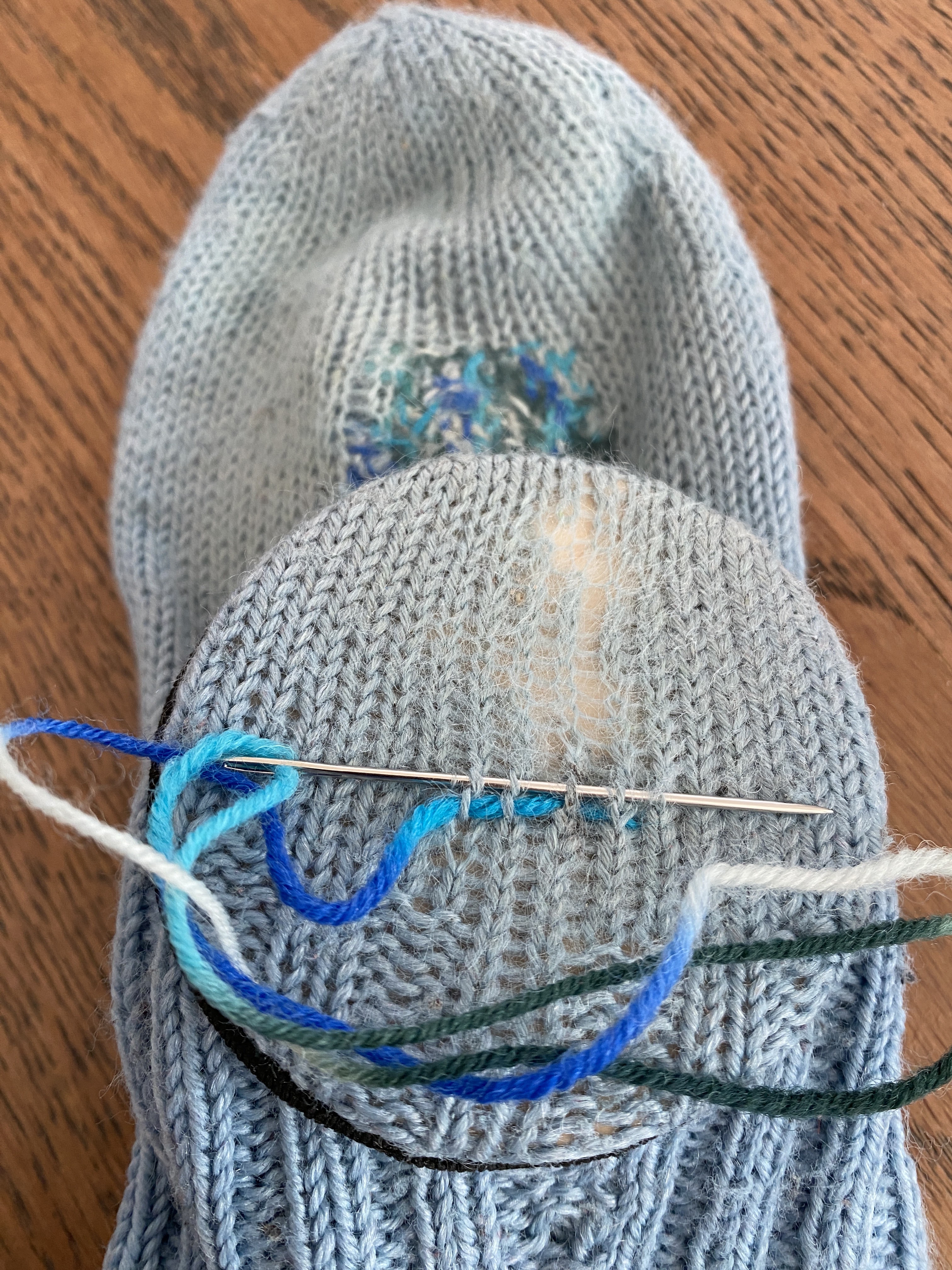 Kuvassa sukan kantapäässä langat ovat jo kuluneet melkein puhki. Sukka on aloitettu parsia vahvemmaksi sinisellä liukuvärilangalla.