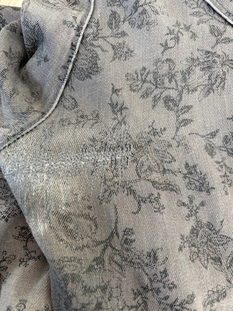 Lähellä oleva kuva vaaleasta farkkukankaasta, jossa on tummanharmaa kukkakuvio ja jota on korjattu ompelukoneella edestakaisin ommellen suorilla ompeleilla samaan sävyyn.