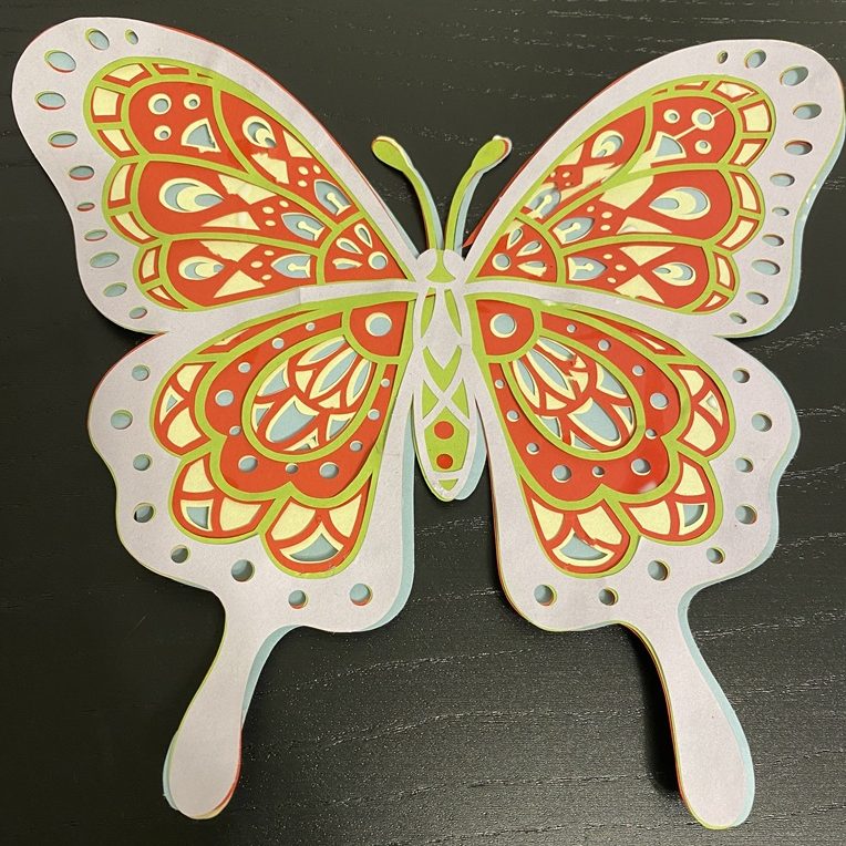 Monen kerroksen värikäs perhonen tehty kartongista. Aukoista näkyy aina alemman kerroksen väri läpi.